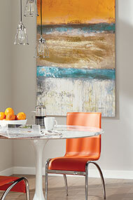 Bright colored artwork on wall with orange chair and glass table